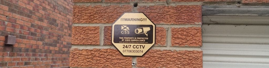 a warning sign that mentions the property is being monitored with a 24/7 CCTV camera