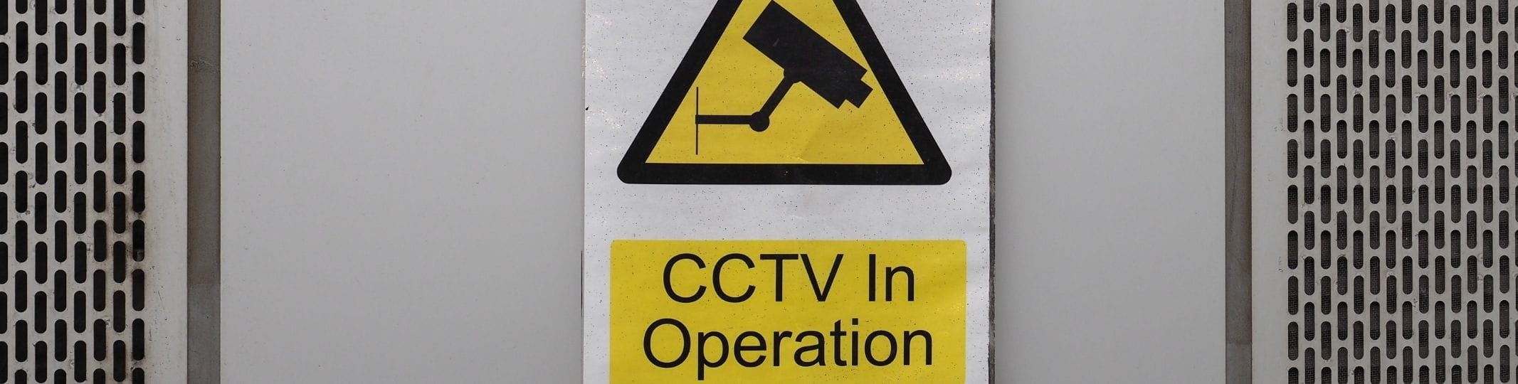 Yellow and black CCTV In Operation warning sign mounted on the exterior wall of a building